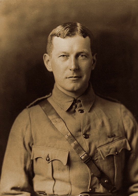 Sepia portrait of John McCrae in military uniform with a leather cross strap, photographed around 1914.